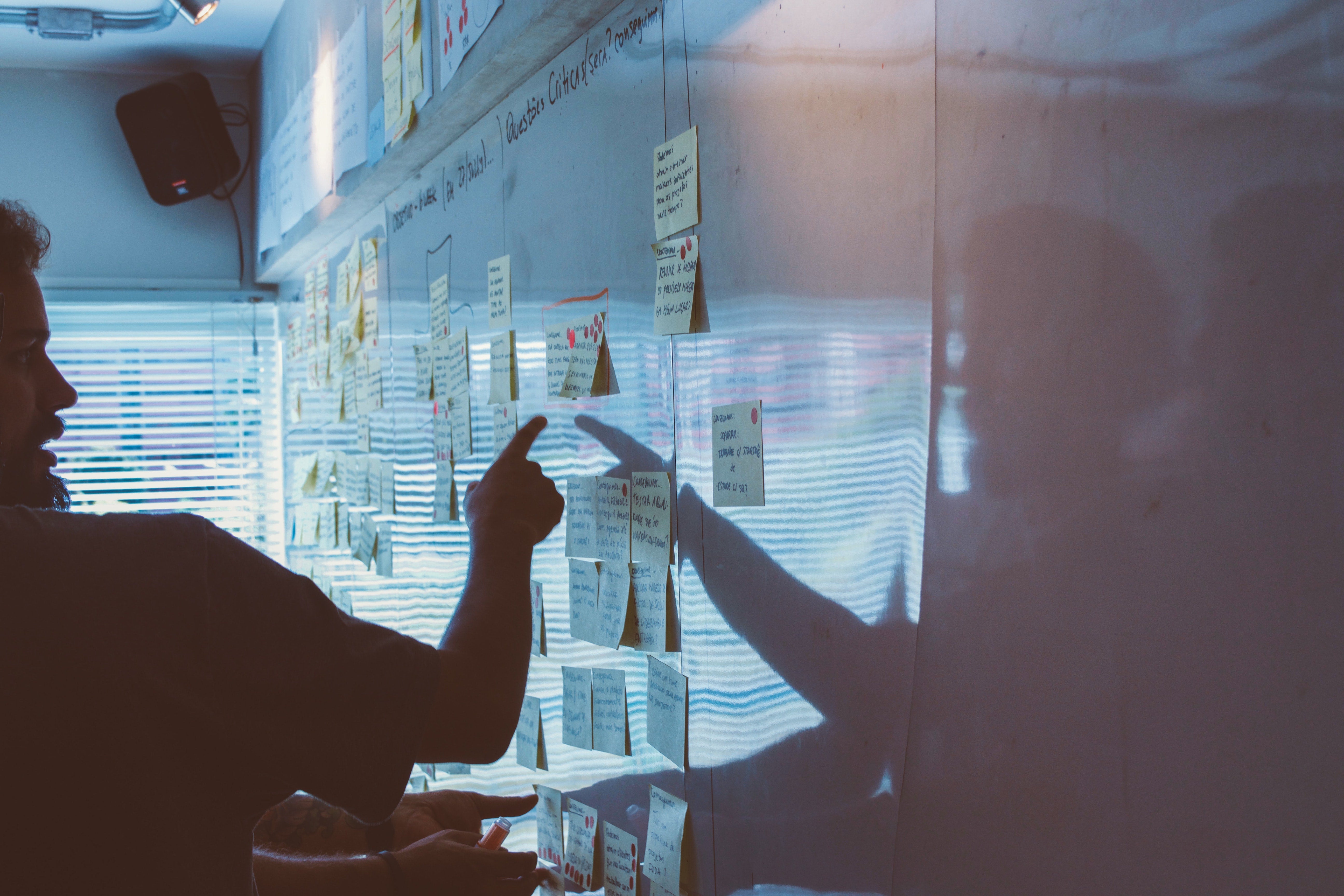 A picture of a man pointing to post-it notes on a whiteboard.